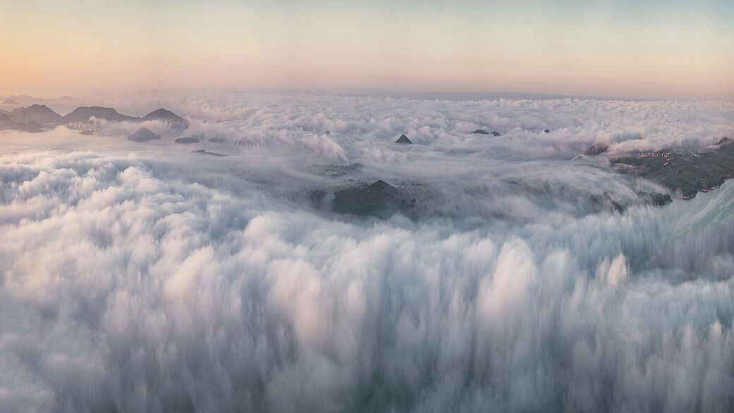 A sea of fog below a viewpoint at sunrise, with hilltops poking through.